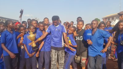 A group of students in blue jerseys posing with a gold trophy.