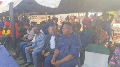 Guests seated on benches under the marquee watching the sports day.