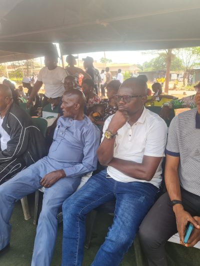 Two men seated side by side under the marquee watching the sports day.