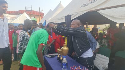 A guest in a green shirt shaking hands with an organiser as a trophy is presented.