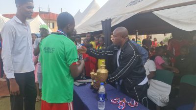 A man in a green shirt being handed a gold trophy under the event marquee.