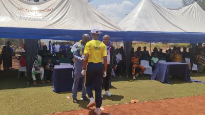 A man in a yellow shirt and white cap standing on the field near the marquees.