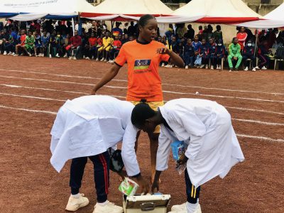 Two students in white shirts unpacking equipment from a case on the running track while a pupil in an orange vest looks on.
