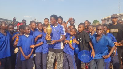 Students in blue jerseys holding a large gold trophy together.
