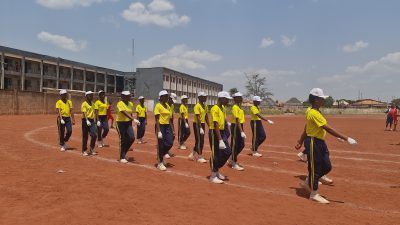 The school band in yellow shirts marching on the track carrying drums and a banner.