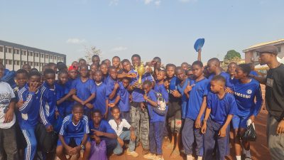 Students in blue jerseys holding up gold trophies and cheering on the field.
